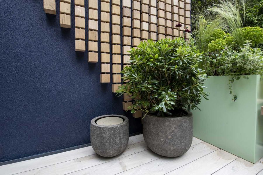 2 granite pots, 1 planted, sit on Polar DesignBoard composite decking, in corner formed by metal raised bed and blue wall.