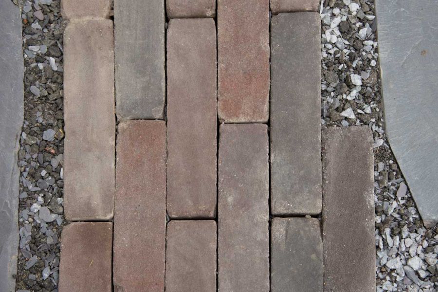 Close view of Bergamo clay paving bricks laid running bond in gravel, showing red and grey tones. Free UK delivery available.
