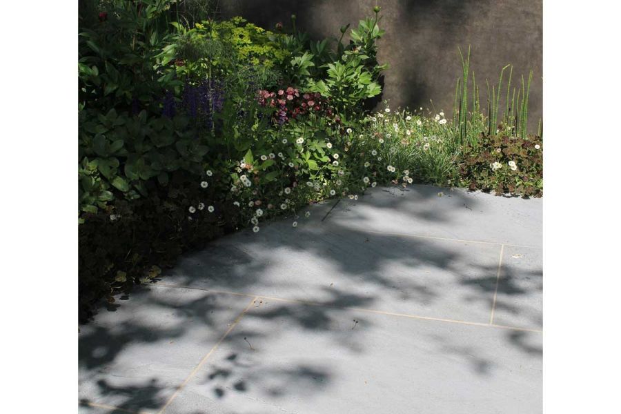 Kirkby Porcelain outdoor tiles, laid in running bond patter, in shady corner, edged with erigeron, taller plants behind.