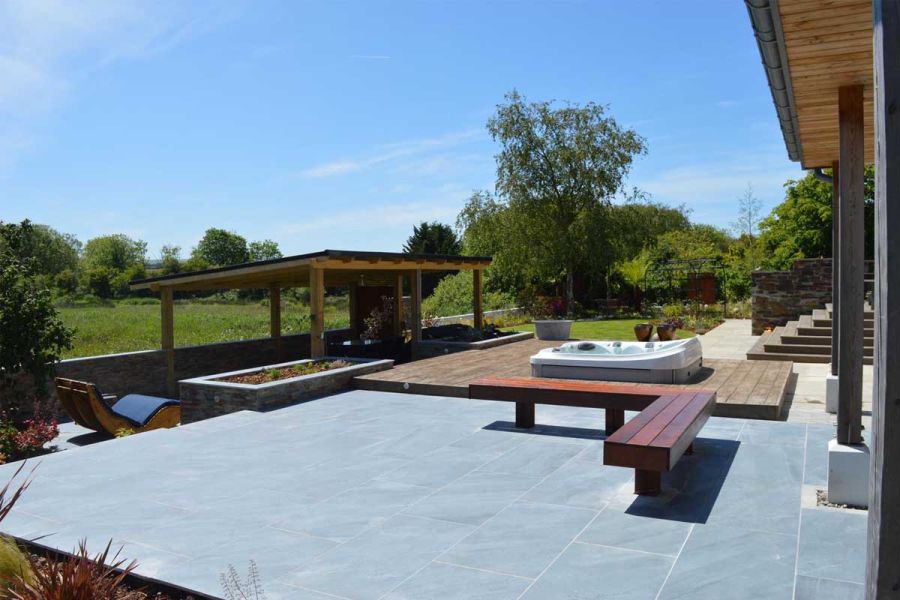 Large patio terrace overlooking field and trees, paved in Kirkby Porcelain tiles, next to hot tub set into decking.