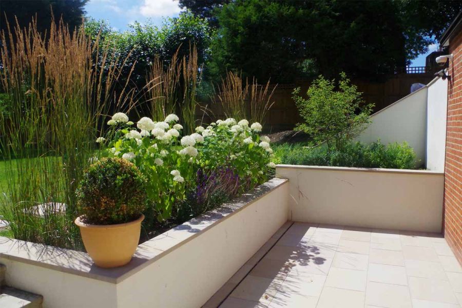 Buff sandstone smooth paving slabs, bounded by house and 2 walls retaining beds and lawn behind. Design by Kiwi Landscapes.