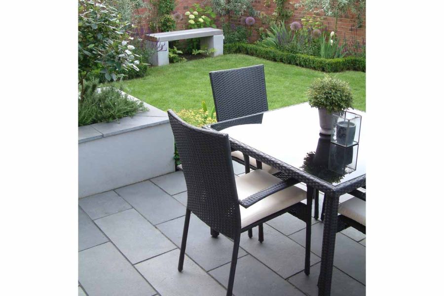Outdoor furniture sits on Kota Blue limestone paving, next to lawn and raised bed with matching coping. Brick wall edges garden.