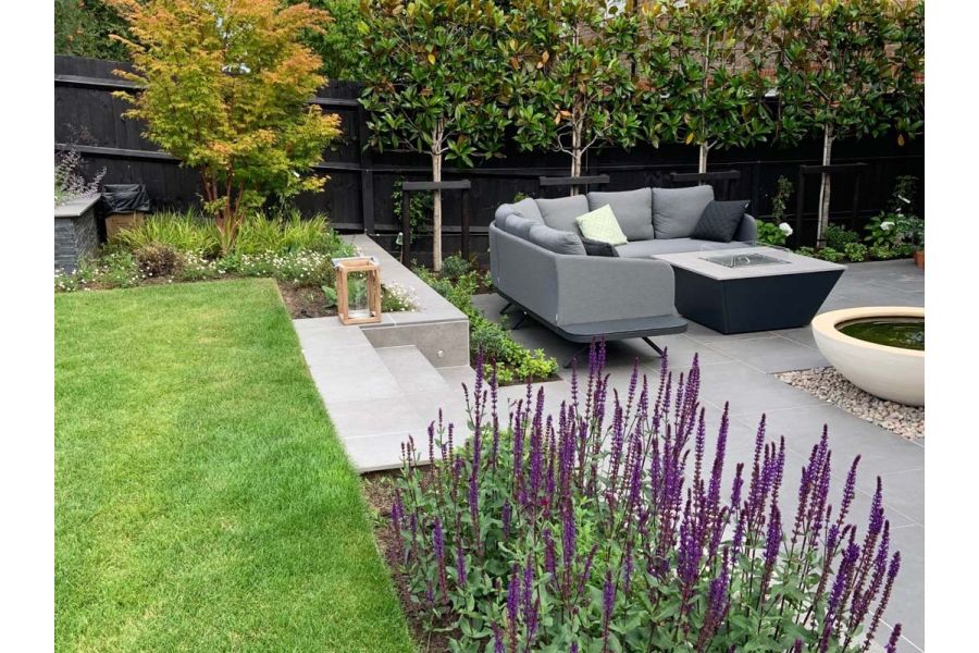 Raised lawn area surrounded by flower beds  and looking down onto a Steel Grey porcelain patio and lounging furniture.