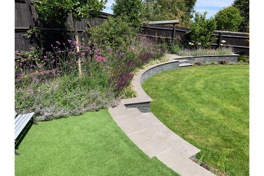 Large circular lawn bordered by curved retaining wall and steps. Steps and wall copings made from Steel Grey porcelain.