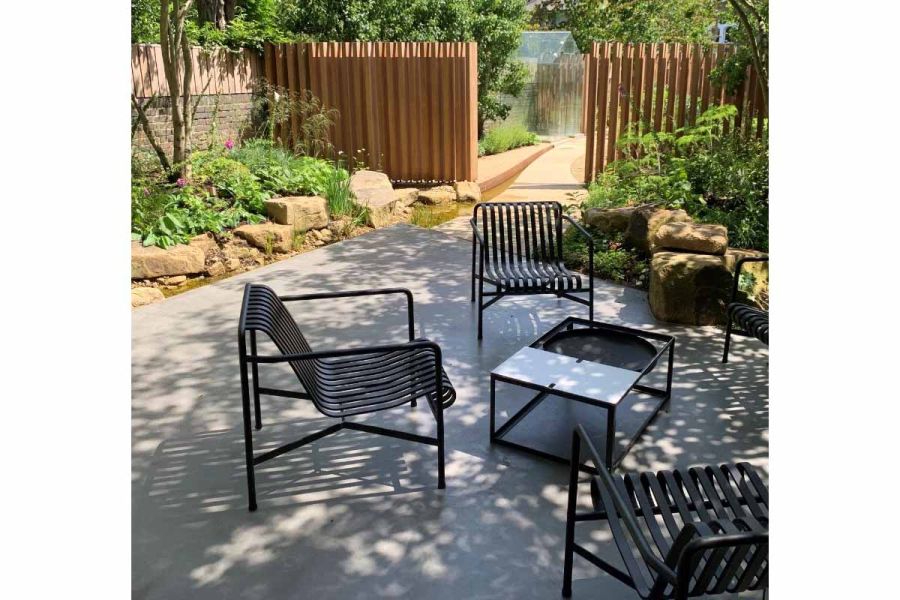 3 metal chairs and fire bowl table on Britannia Buff sawn Yorkstone paving, with borders of small sandstone boulders and planting.