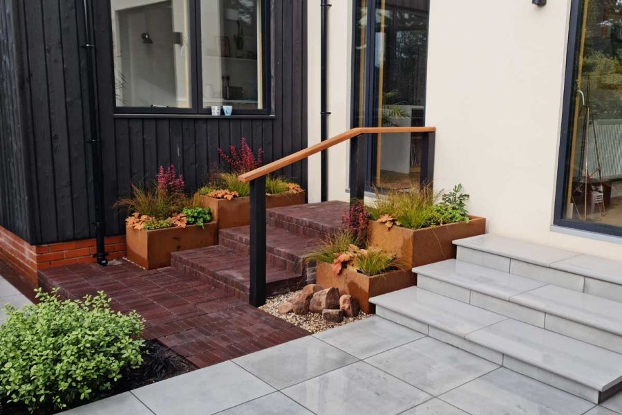 3 shallow steps of Bolzano Dutch clay pavers with wooden handrail rise to glass door. Design by Jane Houghton. Built by Landigo Ltd.