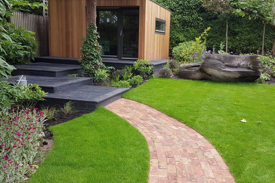 Curved Cotswold Blend clay brick path meets 3 deep square overlapping steps up through planted border to garden room.