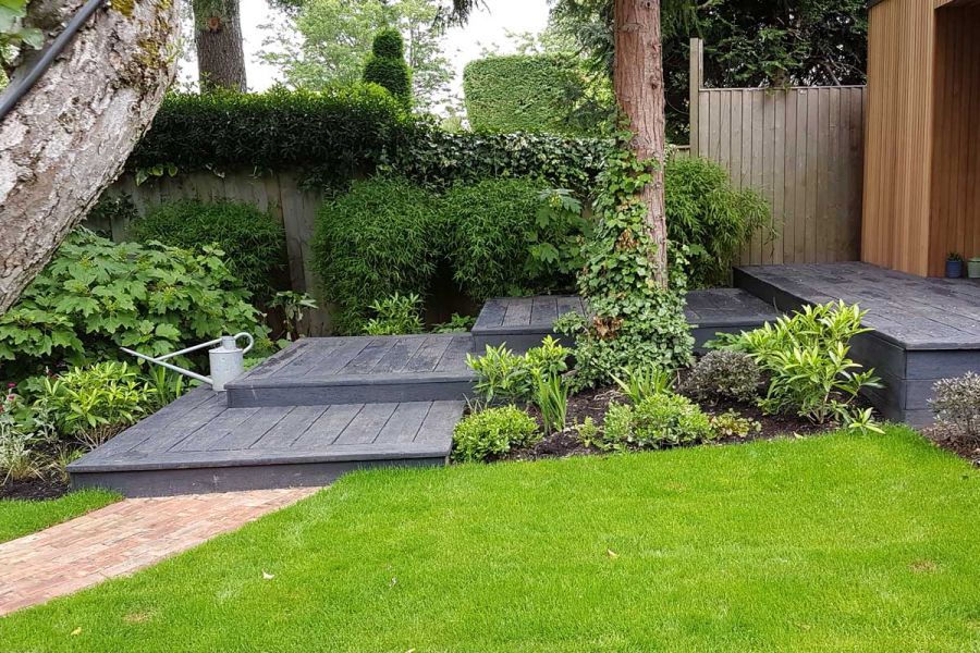 3 large overlapping platforms of Embered Millboard decking ascend to matching patio edged with planted borders.