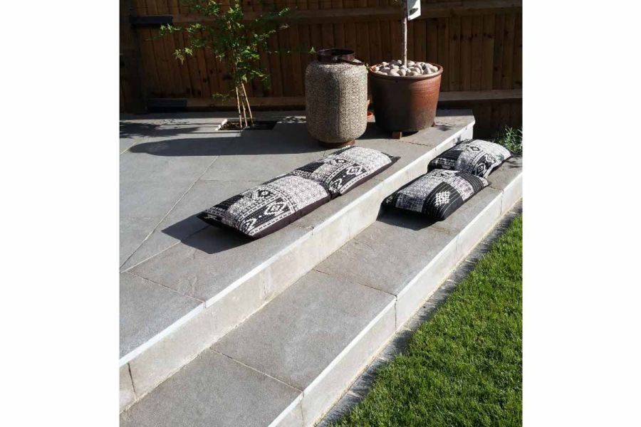 4 pillows lying on edge and step down from Graphite Grey limestone patio laid with acute-angled corner by fence.