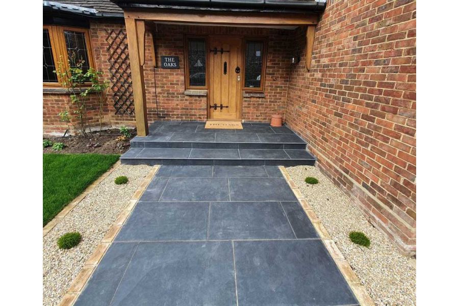 Charcoal Porcelain outdoor tiles laid between gravel beds as wide path, 2 steps and floor of open porch of house named The Oaks.