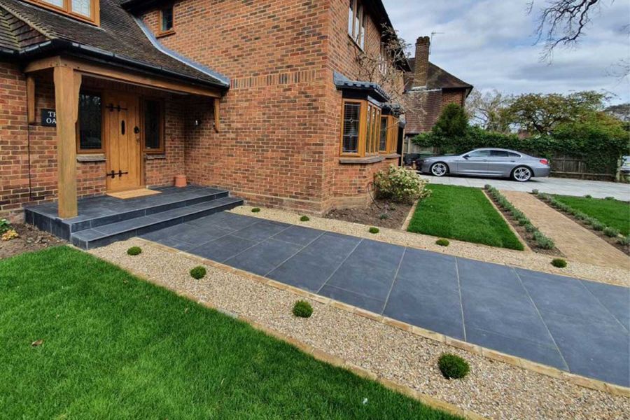 2 wide Charcoal Porcelain bullnosed steps up from path in matching paving to open, timber-pillared porch of brick suburban house 