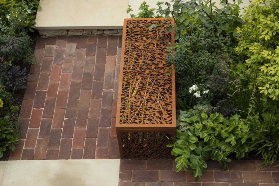 Pierced rusted steel decorative gabion edges bed of small shrubs next to paved areas of slabs and Dorset Antique Belgian bricks.