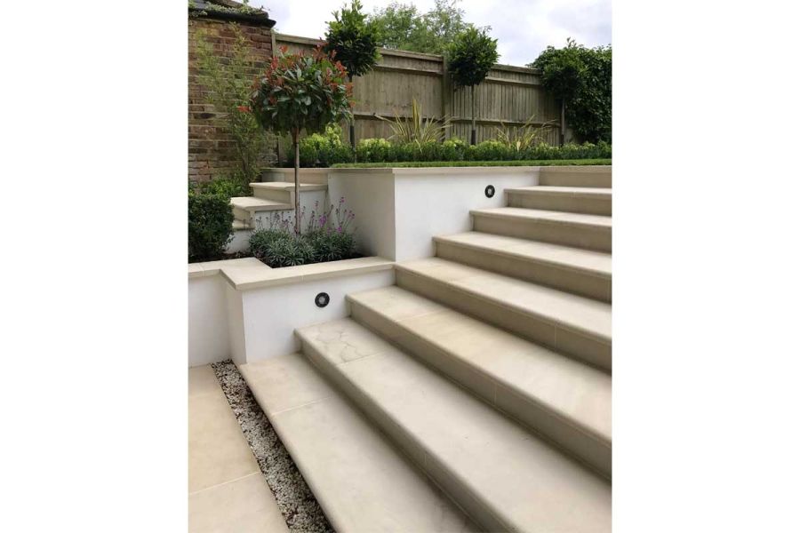 8 Beige Sawn Sandstone bullnose steps, with gravel strip at base, rise to lawn from matching paving. By Landscape Design Studio.