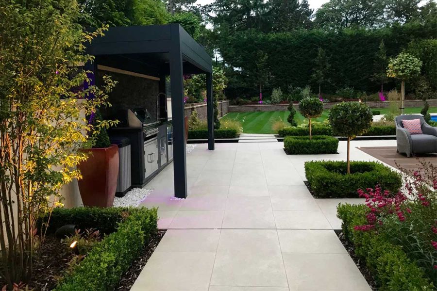Outdoor kitchen area with square planted beds set into Golden Stone porcelain paving. Designed by Landscape Design Studio.