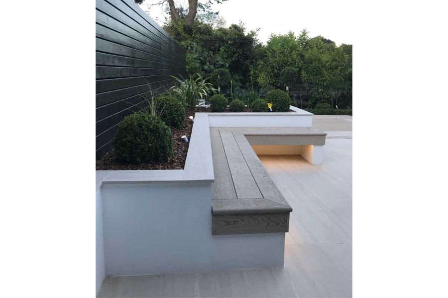 Raised bed, planted with clipped shrubs, with attached L-shaped bench of Limed Oak Millboard Decking. By Landscape Design Studio.
