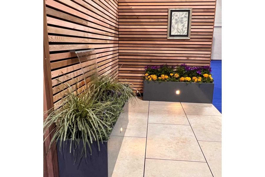 Exhibition stand of a small pocket garden with cedar timber horizontal screens, green fibreglass planters and a Jura Beige Porcelain patio.