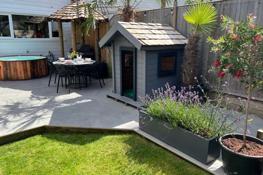 Small urban rear garden with larged paved area, circular hot tub, table and chairs, and covered barbecue space.