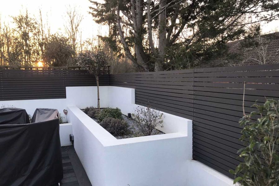 Long white raised bed with small tree sits on patio in corner formed by fence of Dark Ash composite screening.