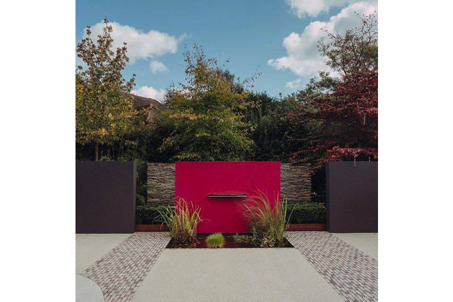 Strips of Silver Grey Multi clay pavers run either side of water feature with red wall and planted pond. Built Langdale Landscapes.