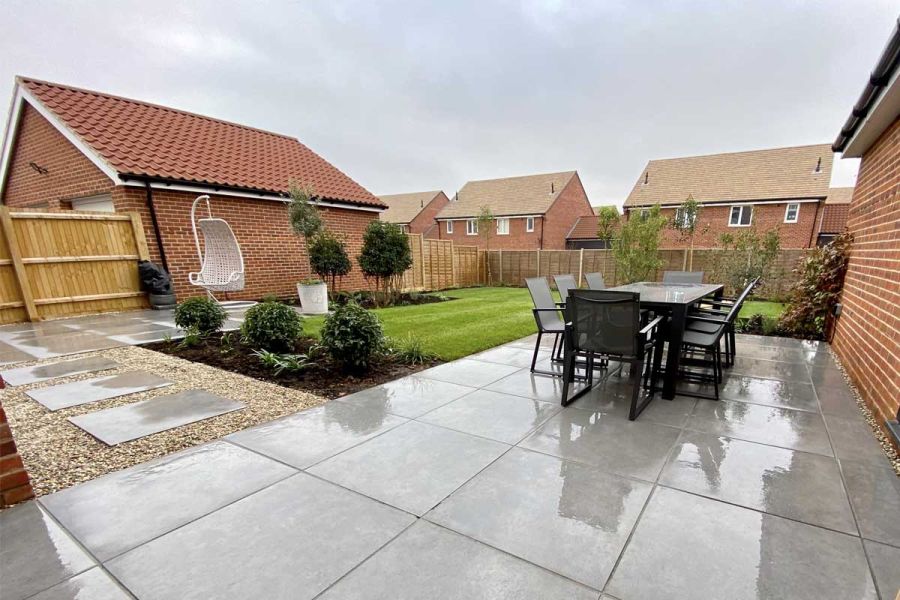 Large metal dining set on Anthracite 800x800 large patio slabs next to lawn, with gravel and porcelain tile path to swing chair.