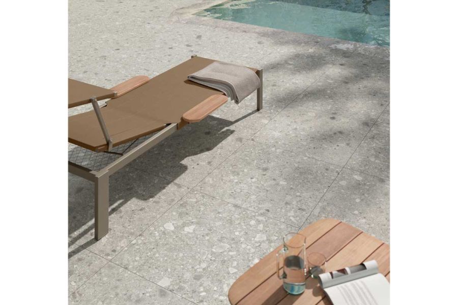 Lounger sits on Brera large porcelain paving slabs by side of swimming pool. 