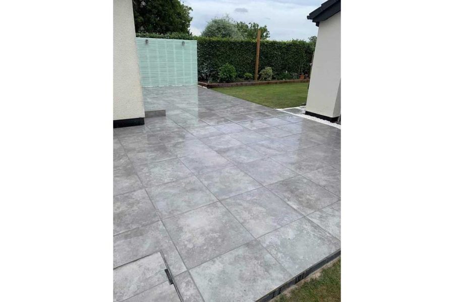 Wrap-around patio of 600x600mm Silver Contro Porcelain paving laid in stack bond, with lawn and battened screen in background.