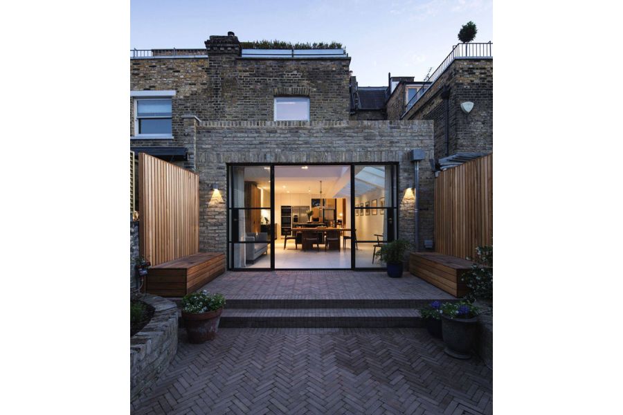 Rear of terrace property with large extension with picture window opening onto narrow garden paved with Westminster brick pavers.