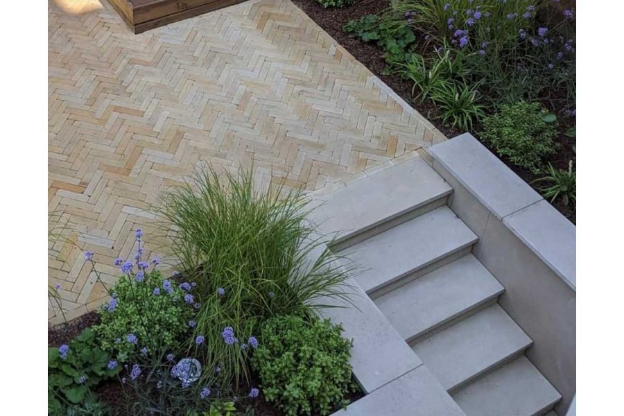 From herringbone-pattern clay-paved area, 5 grey steps descend between flanking walls faced with Golden Sand DesignClad.