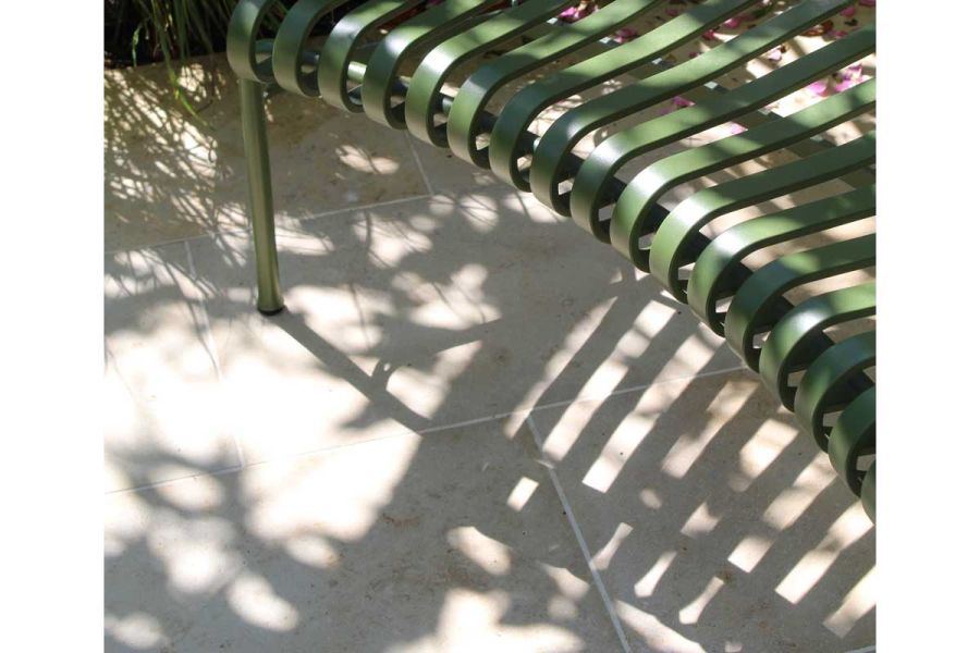 Curved green metal slatted bench casts shadow on Jura Beige sawn limestone slabs in Leon van Rooyen Design.