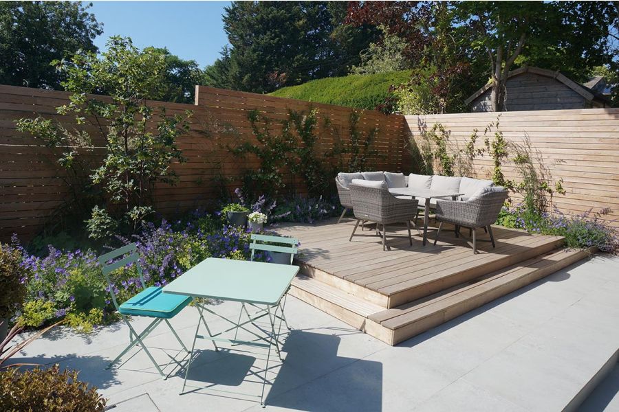 Raised decking seating area surrounded by colourful flower beds and a Light Grey Porcelain paved patio.