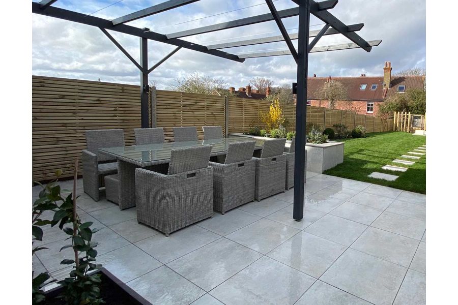 Low maintenance family dining area on top of a Porcelain patio with a metal pergola above and cladded raised beds.