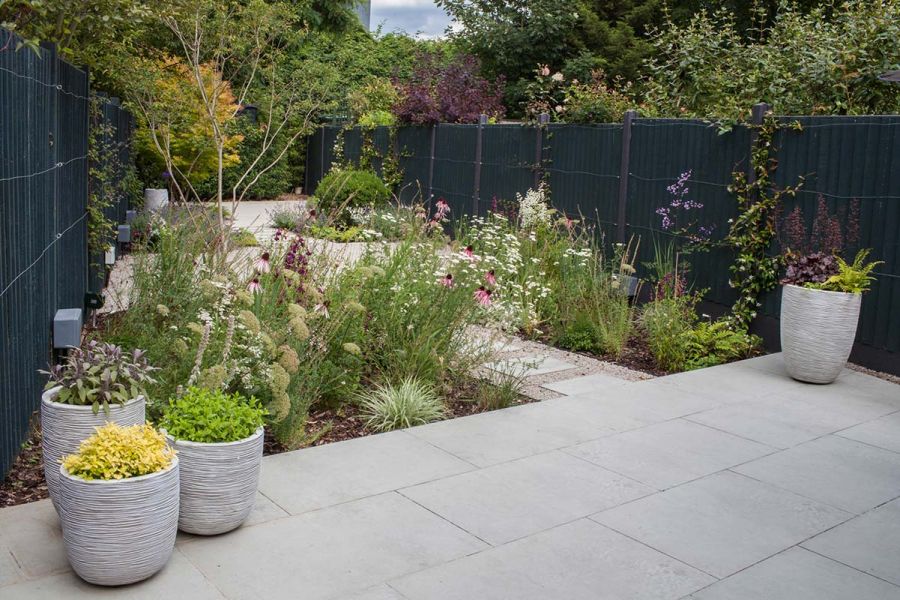 Narrow rear garden with multiple paved porcelain patios linked together by porcelain stepping stones and planted flower beds.