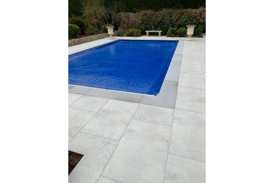 Large rectangular swimming pool with contrasting coping stones and an adjoining patio of large porcelain paving slabs.