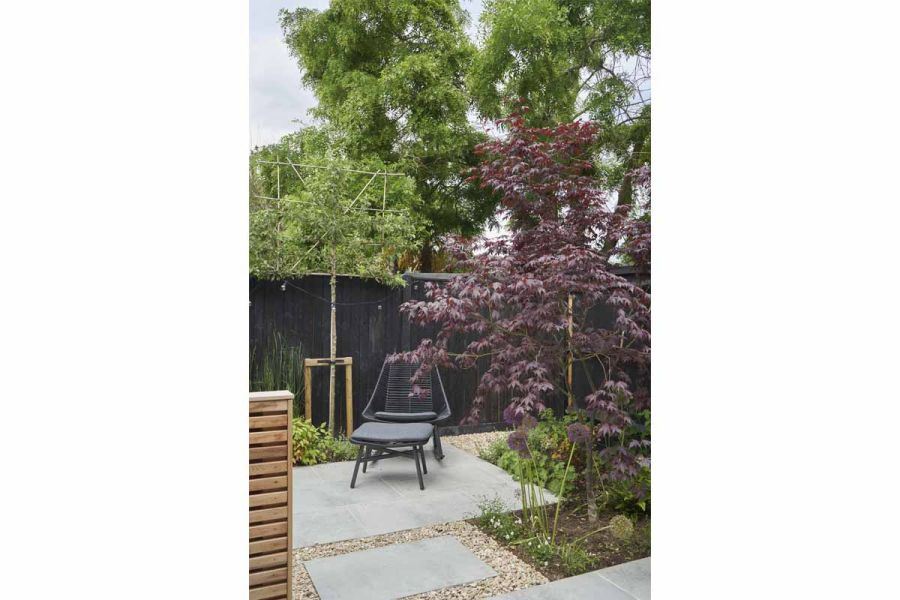 Modern garden scheme with Light Grey porcelain paving and luxury garden chair with footstool, surrounded by mature planting.
