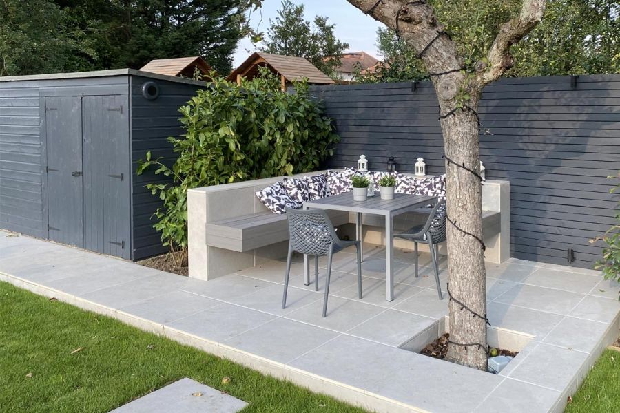 Raised Florence Grey Porcelain paved dining area next to painted fence. Bench cantilevered into wall on 2 sides of metal table.