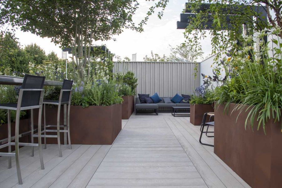Rectangular outdoor space with Corten steel planters, sofa and bar seats, decked with Limed Oak Millboard composite boards.