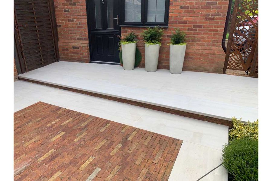Faro Porcelain Paving teamed with clay pavers used with downstand steps, one leads up to door where 3 planters sit next to it.