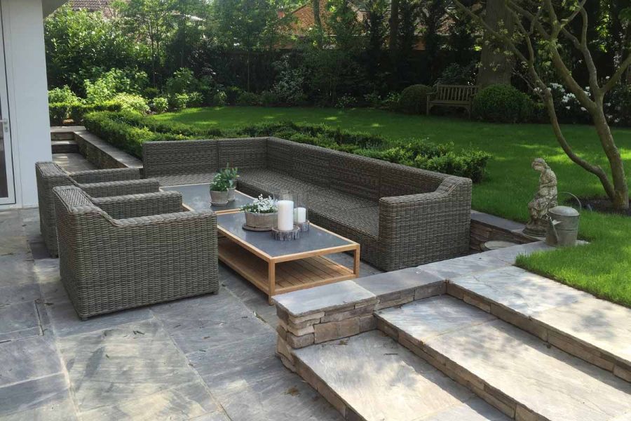 Large lounge set on patio of Tumbled Black Indian sandstone paving with 3 wide shallow steps up to lawn in shady fenced garden. 