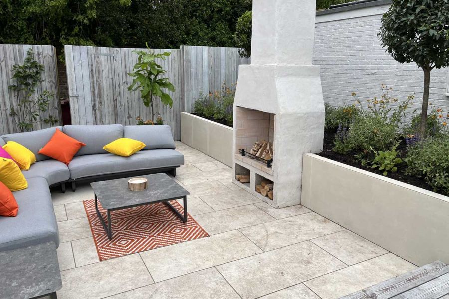 L- shaped sofa and table in front of outdoor fireplace with chimney set into raised bed faced with Desert Beige exterior cladding.