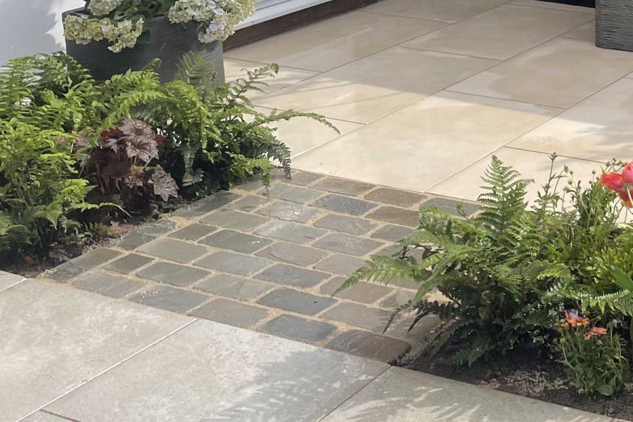 Strip of 8 rows of Kandla Grey tumbled cobble setts between 2 colours of paving, bordered by ferns. Built by J P Landscapes.