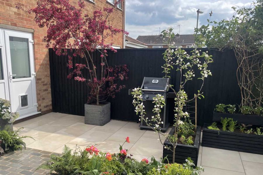 Low maintenance rear garden with a Venetian Beige Porcelain patio, black painted fence panels and raised planter beds.
