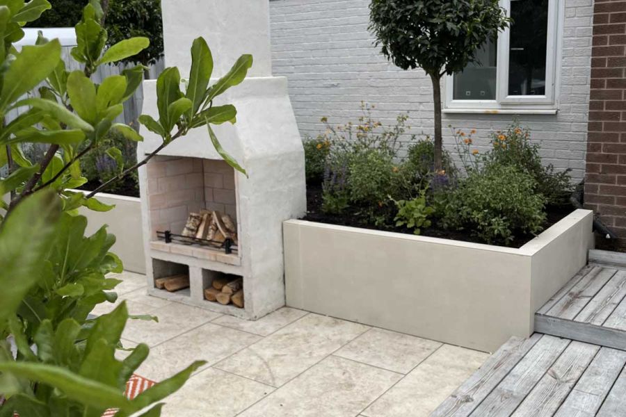 Step down from decking to paved area with outdoor fireplace set into raised bed faced with Desert Beige exterior cladding.