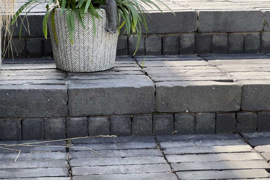 Close view of steps of Lucca brick paving, pavers laid stack bond with risers of cut bricks laid vertically. Plant in pot to left.