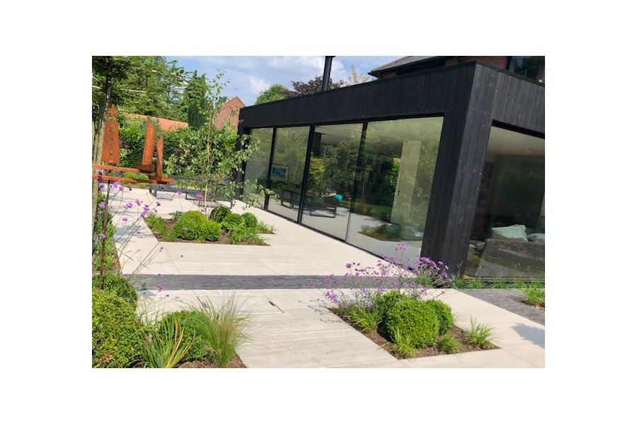 Modern glass-fronted extension faces onto paved patio interrupted by strips of Lucca clay bricks and rectilinear beds.