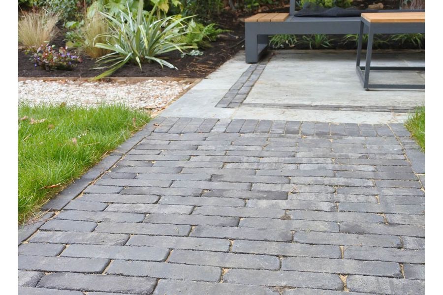 Path of Lucca Dutch clay pavers, between lawns, meets rectangular paved area with brick detail and outdoor furniture.