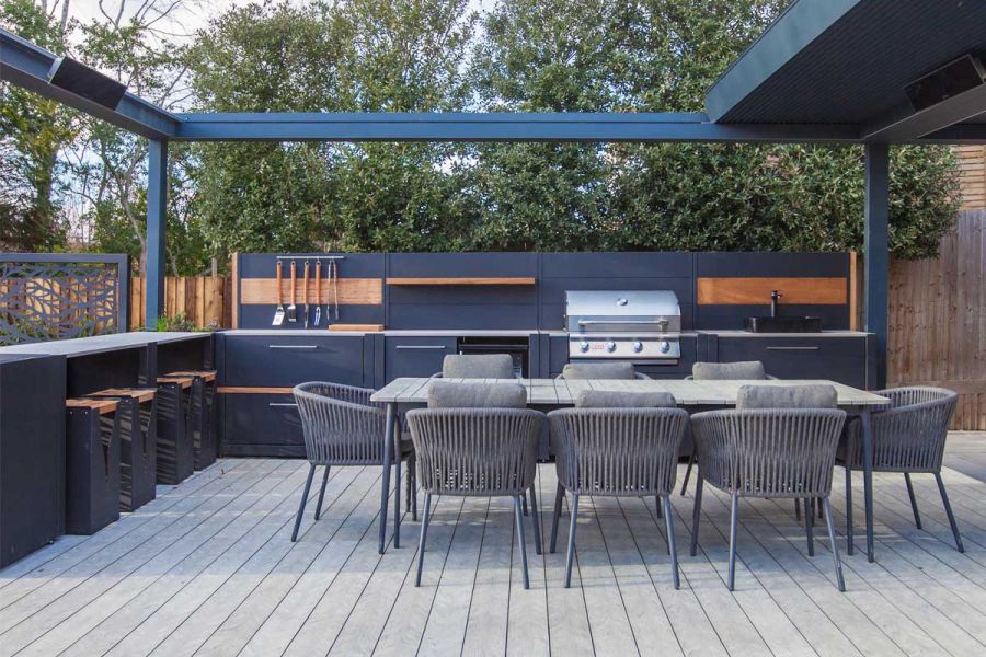 8-seat outdoor dining set on Luna DesignBoard decking, under pergola with outdoor kitchen on 2 sides. Built by Graduate Landscapes.