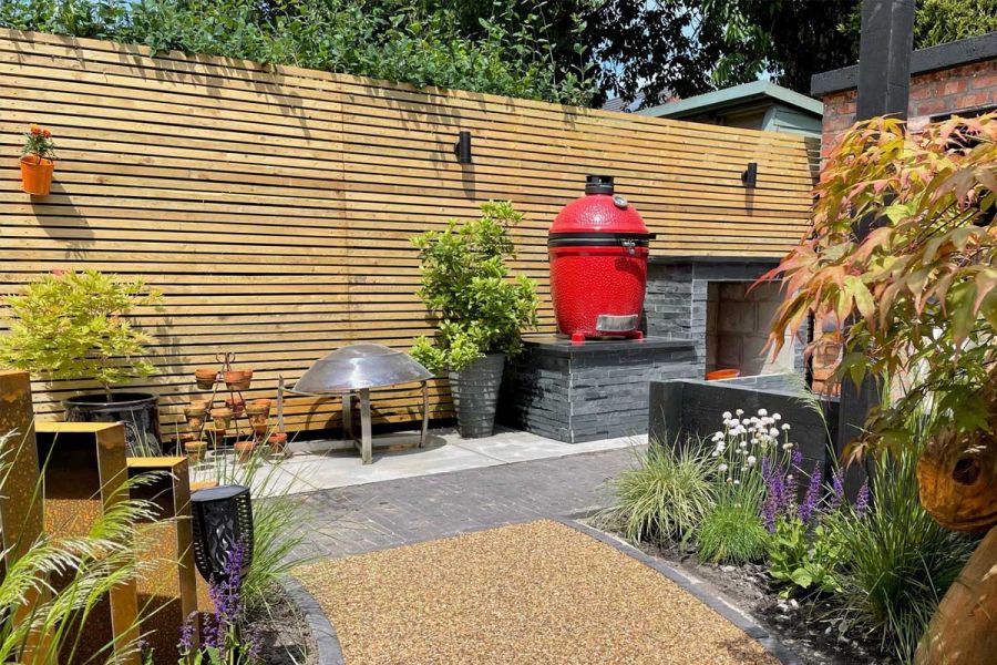 Outdoor kitchen area with path of charcoal grey clay pavers running through it. Red bubble BBQ stands out against cedar fencing.