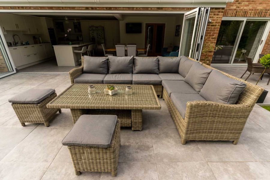 Luxury rattan garden furniture with brown cushions on Silver Contro porcelain patio, in front of kitchen with open bifold doors.