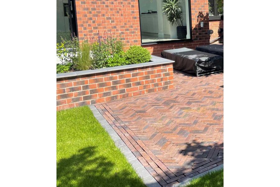 Floor-length windows overlooking brick raised bed, grass and Vulcano Clay Pavers laid herringbone by Lynn Cordall Landscapes.