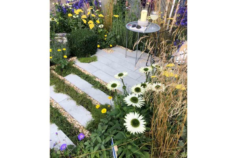 Alternating lines of slabs, gravel and low planting lead between daisy-like flowers to tiny patio of Light Grey porcelain planks.